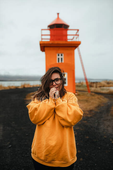 Glückliche Frau steht nahe orangefarbenem Leuchtturm am Meer — Stockfoto