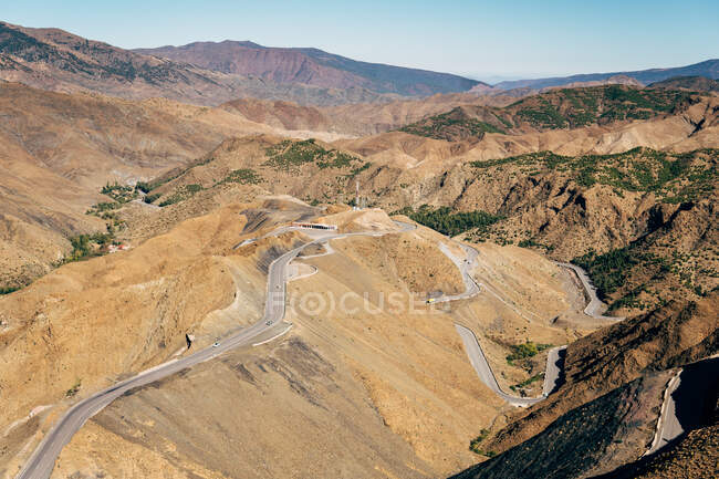 З верху порожньої асфальтової звивистої дороги на потужних брунатних пагорбах у сонячний день у Марокко. — стокове фото