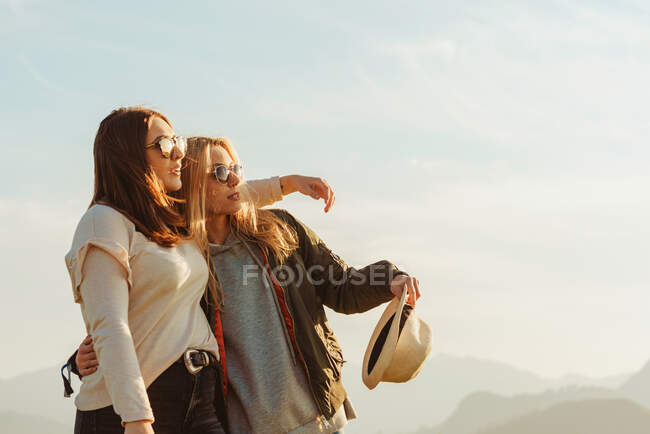Vista lateral de las mujeres abrazándose en el campo y mirando hacia otro lado - foto de stock