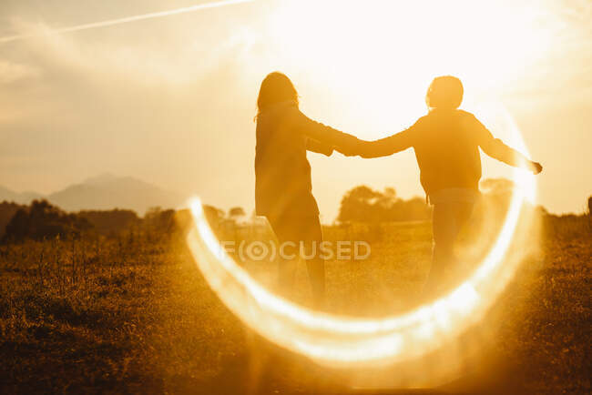Girlfriends holding hands gently standing in lens flare of sunset light in nature — Stock Photo