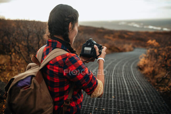 Back view of young tourist on walkway taking photo of valley from hill and cloudy sky — Stock Photo