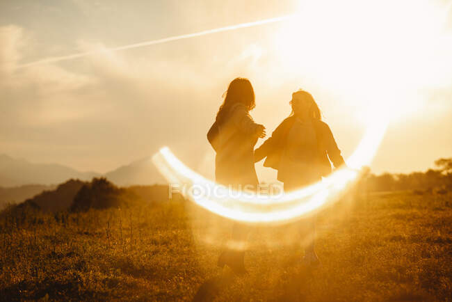 Girlfriends standing in lens flare of sunset light in nature — Stock Photo
