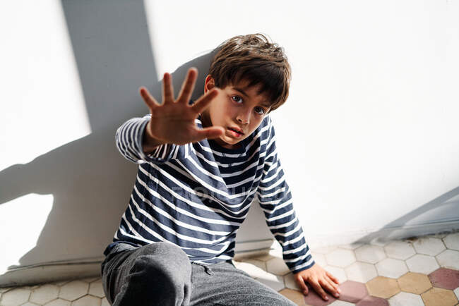 Unhappy preteen ethnic boy sitting on floor and outstretching arm while trying to protect himself from angry parent — Stock Photo