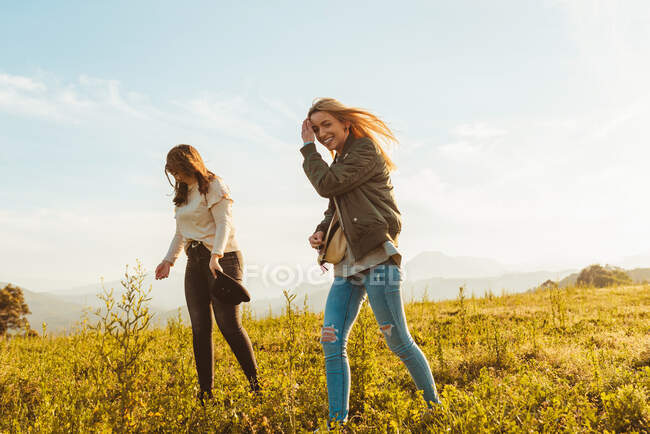 Niedriger Winkel lachender Frauen, die gemeinsam im Sonnenlicht auf der grünen Wiese im Gebirgstal spazieren — Stockfoto