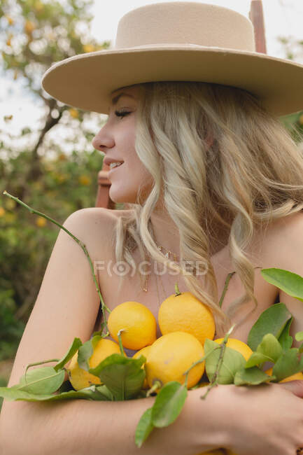 Donna positiva in piedi con agrumi in mano nel frutteto durante la stagione della raccolta — Foto stock