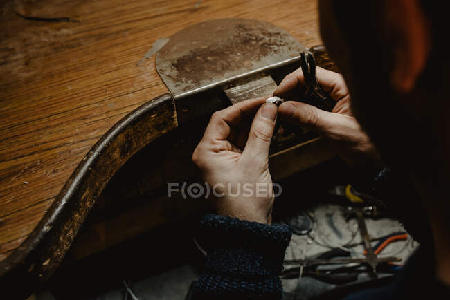 Gioielliere maschio anonimo che utilizza il file per modellare l'anello metallico sul banco da lavoro in officina — Foto stock