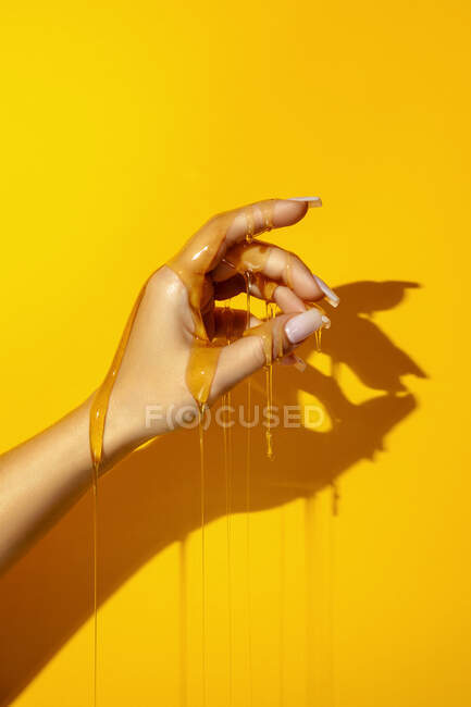 Врожай невизначена жінка, що демонструє руку з манікюром та ароматичними медовими рідинами на жовтому тлі з відтінком — стокове фото