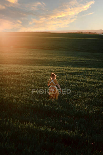 Молодая женщина в винтажном деревенском стиле платье работает в одиночку на обширном зеленом травянистом поле в летний вечер в сельской местности — Stock Photo