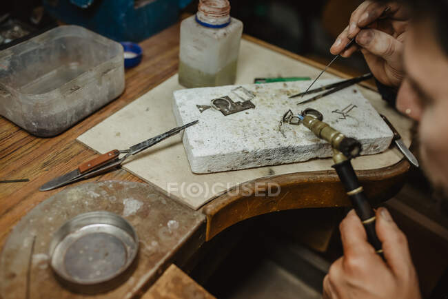 Anonymer Goldschmied erhitzt winzige Metallornamente mit Pusteblume, während er Schmuck auf Werkbank herstellt — Stockfoto