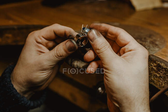 Анонімний ювелір тримає незакінчене кільце в брудних руках і перевіряє якість в майстерні — стокове фото