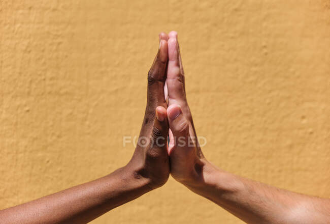 Vista laterale di crop anonimi amici multietnici tenere le mani insieme in alto cinque gesto contro il muro giallo — Foto stock