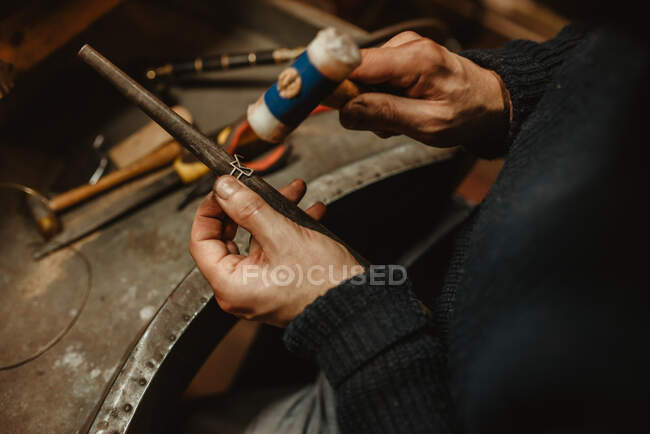 Anonyme orfèvre martelant et élargissant anneau blanc sur bâton de métal tout en travaillant dans l'atelier — Photo de stock