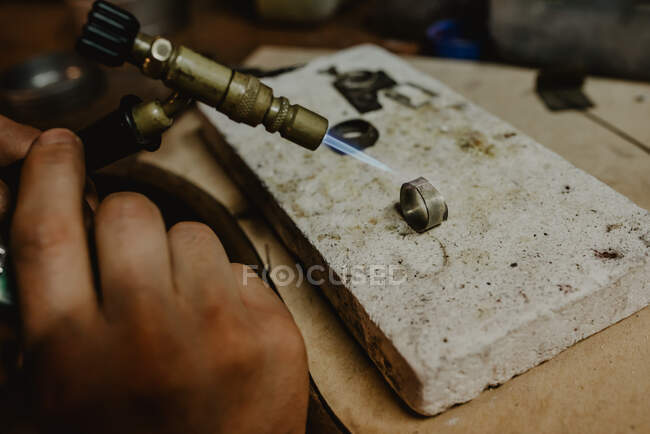 Анонимный мужчина-ювелир, использующий файл для формирования металлического кольца на верстаке в мастерской — стоковое фото