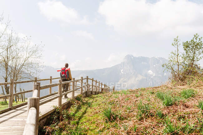 Back view of unrecognizable explorer with backpack walking on wooden pathway in mountainous terrain — Stock Photo