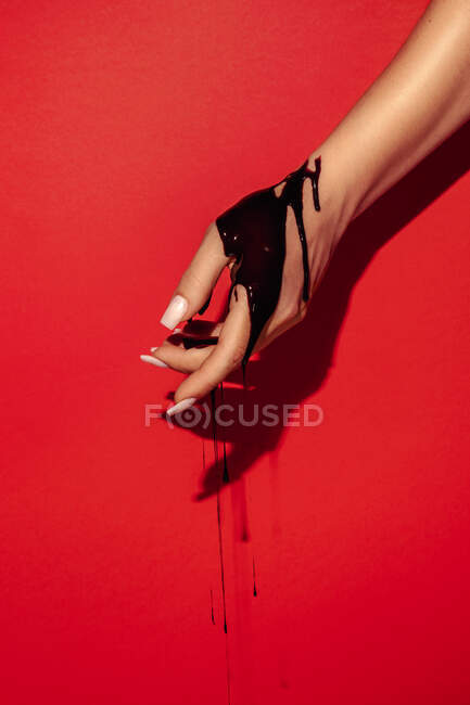 Cortar fêmea irreconhecível com manicure e fluxos de tinta preta na mão sobre fundo vermelho com sombra — Fotografia de Stock
