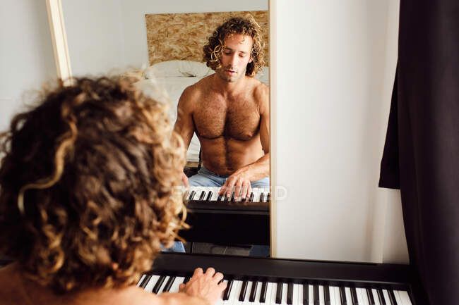 Dall'alto bel musicista maschio senza camicia che suona la melodia al pianoforte mentre prova a casa davanti a uno specchio — Foto stock
