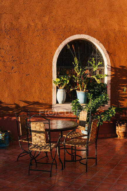 Cómodas sillas alrededor de la mesa en una elegante terraza decorada con plantas verdes durante la noche soleada en Marruecos - foto de stock