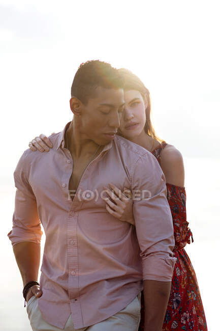 Liebevolle Frau umarmt schwarzen Mann von hinten, während sie den Sommertag zusammen am Strand verbringt — Stockfoto