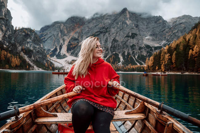 Mujer sonriente en barco de madera con remos flotando en aguas turquesas de lago tranquilo en el fondo de majestuoso paisaje de las tierras altas en Dolomitas en Italia alpes - foto de stock