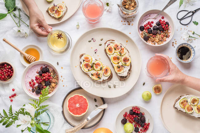 De acima de pessoas anônimas que tomam xícaras de bebidas saudáveis frescas da mesa com comida variada para o café da manhã — Fotografia de Stock