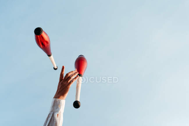 From below of crop anonymous circus artist performing trick with juggling clubs against blue sky — Stock Photo