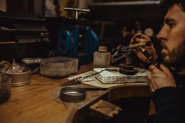 Orfèvre utilisant le chalumeau pour chauffer de minuscules ornements métalliques tout en faisant des bijoux sur l'établi — Photo de stock