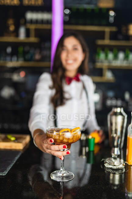 Camarera irreconocible borrosa en traje elegante que sirve cóctel con cáscara de limón mientras está de pie en el mostrador en el bar moderno - foto de stock