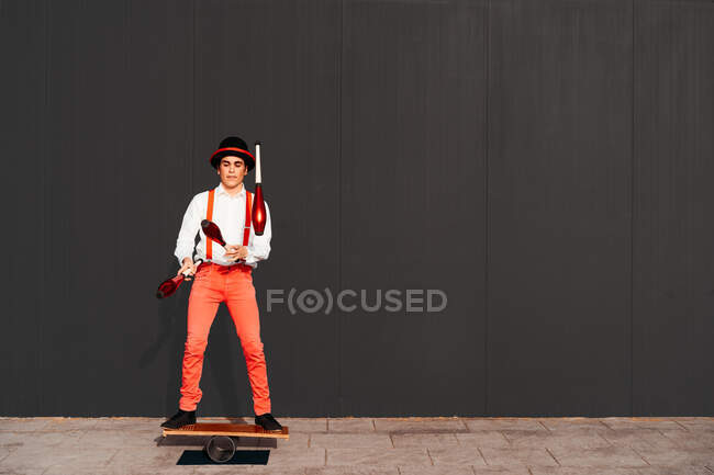Full body of agile professional young male circus performer juggling clubs and balancing on board — Stock Photo