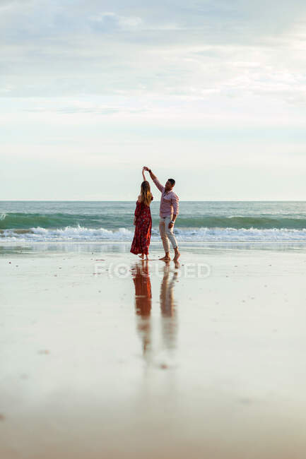 Romantic couple holding hands and dancing together on beach near sea at sunset in summer — Stock Photo