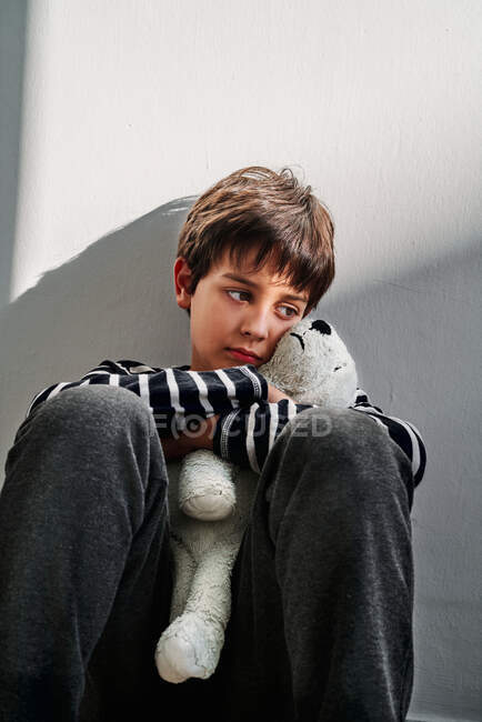 Verärgerter einsamer preußischer Junge, Opfer häuslicher Gewalt, sitzt auf dem Boden und umarmt Spielzeug — Stockfoto