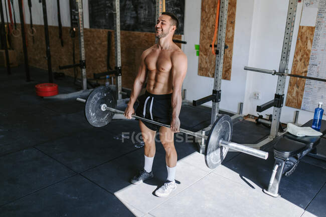 Fuerte atleta masculino haciendo deadlift con pesadas barras durante el entrenamiento en el gimnasio - foto de stock