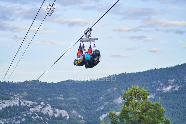 Anonymous brave people in safety equipment riding zip line over mountains in summer — Stock Photo