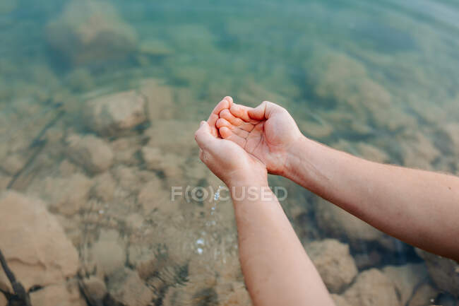 Cultivado irreconocible persona manos sosteniendo el agua de lago transparente - foto de stock