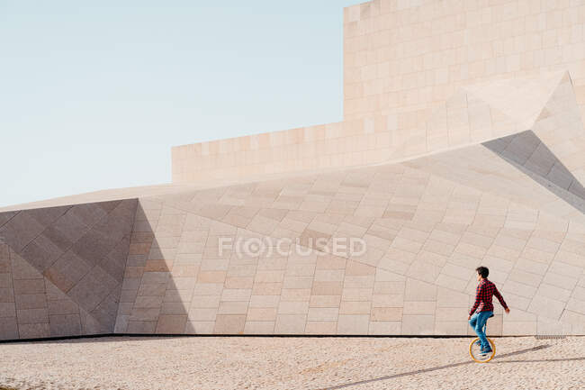 Vista laterale dell'irriconoscibile monociclo maschile contro la costruzione contemporanea in pietra di insolita forma geometrica — Foto stock