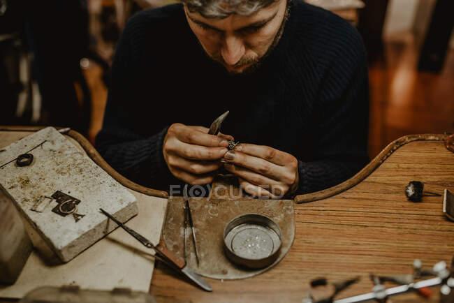 Ювелір тримає незакінчене кільце в брудних руках і перевіряє якість в майстерні — стокове фото