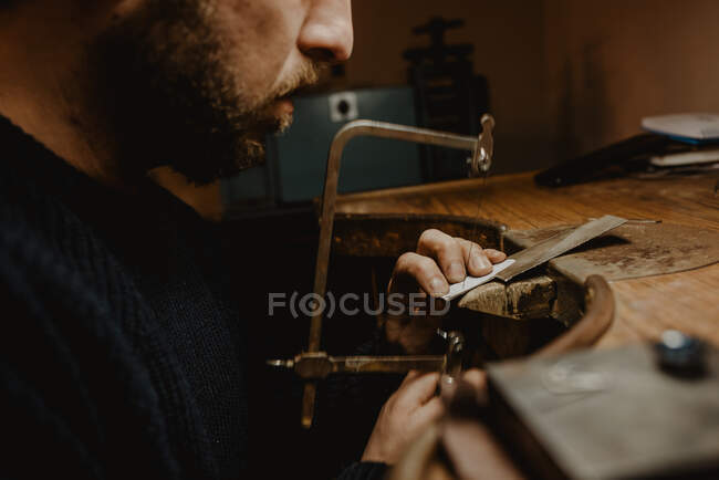 Irreconocible orfebre cortando metal con sierra mientras hace joyas en taller - foto de stock