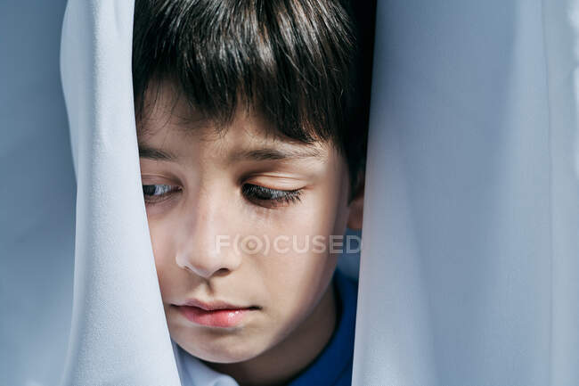 Нещасний маленький хлопчик дивиться з-за штор, страждаючи від домашнього насильства і ховаючись від батьків — стокове фото