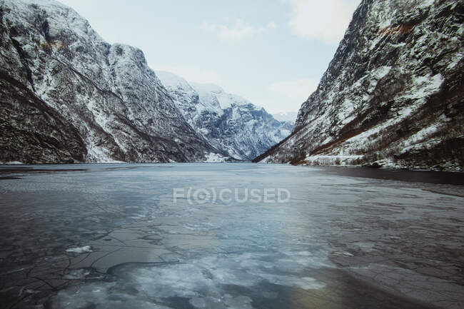 Peak of hill with picturesque view of mountains in snow on shore near water surface — Stock Photo