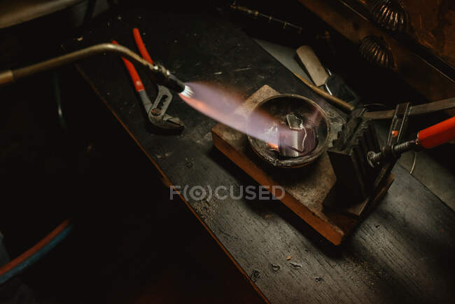Невідомий золотошукач тане метал для ювелірних виробів з паяльною лампою, стоячи поруч з робочою лавкою в майстерні — стокове фото