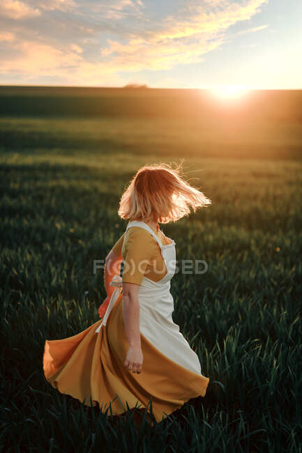 Jovem fêmea em estilo rústico vintage vestido correndo sozinho em vasto campo gramado verde na noite de verão no campo — Fotografia de Stock