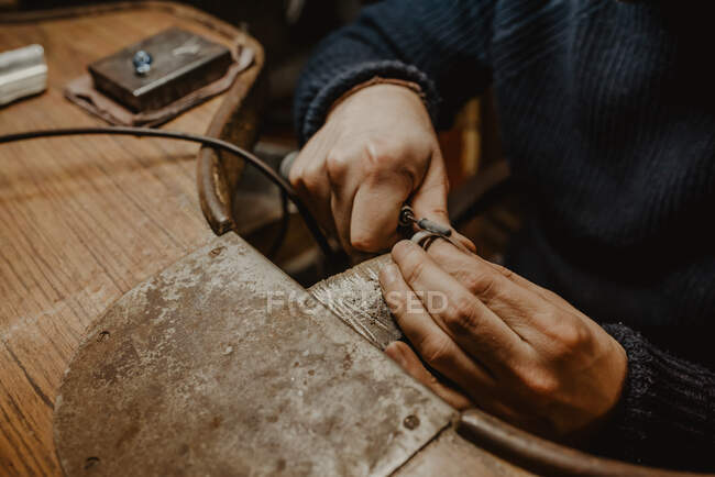 Hands of anonymous male goldsmith using manual tool to shape metal ring in workshop — Stock Photo