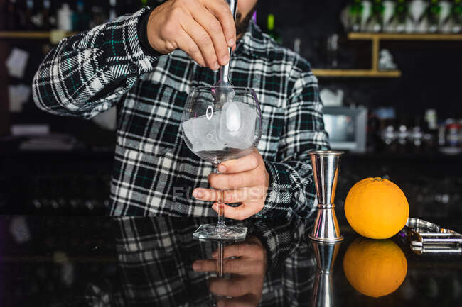 Zugeschnittener, unkenntlich gemachter Barmann bereitet in einem Nachtclub ein alkoholisches Getränk im Glas mit Eiswürfeln zu — Stockfoto
