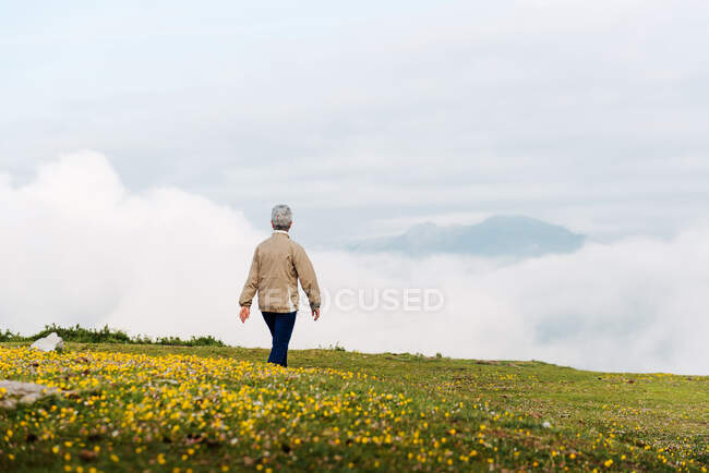 Back view of unrecognizable senior female traveler walking in morning in hilly terrain — Stock Photo