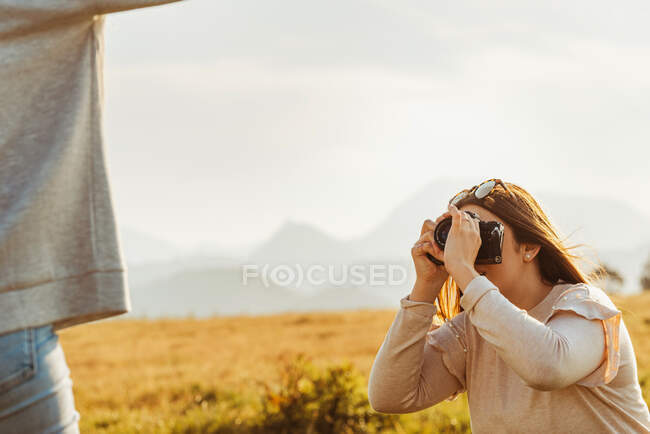 Female taking photo of anonymous girlfriend raising arm and spending time together in mountains — Stock Photo