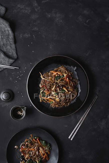 Top view chopsticks and plate with Korean dish Japchae cooked from noodles and vegetables — Stock Photo
