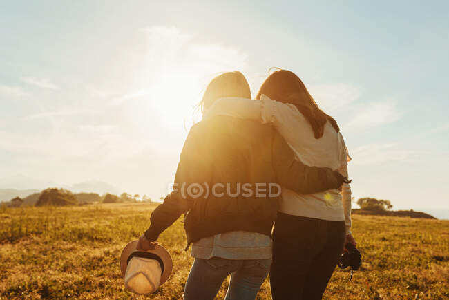 Back view women with photo camera hugging in field — Stock Photo