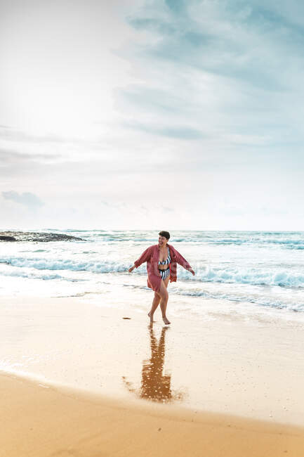 Під час літніх канікул повно босоніж молодої жінки в купальнику, яка прогулювалася вздовж берега моря, обмиті пінявими хвилями. — стокове фото