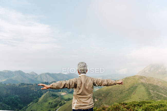 Rückenansicht einer nicht wiederzuerkennenden Seniorin, die morgens in hügeligem Gelände die Arme hebt und ausstreckt — Stockfoto