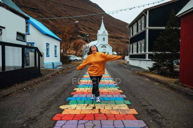 Giovane turista felice con mani ai lati sulla strada tra gli edifici del villaggio vicino alla cattedrale e montagna — Foto stock