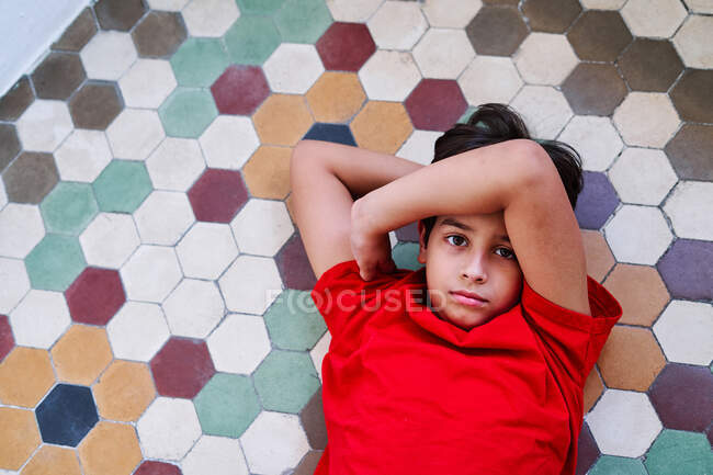 D'en haut de malheureux garçon préadolescent solitaire couché sur le sol en tant que victime de violence familiale et d'abus en regardant la caméra — Photo de stock